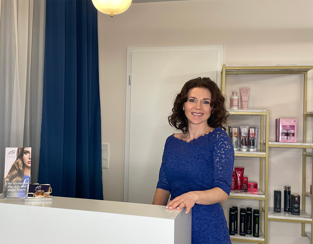 Helene Baumbach, Friseurmeisterin in Neuhofen, steht im ruhigen, persönlichen Salonrahmen ihres Studios mit Haarpflegeprodukten im Hintergrund, bereit für hochwertige Schnitt-, Farb- und Stylingservices.